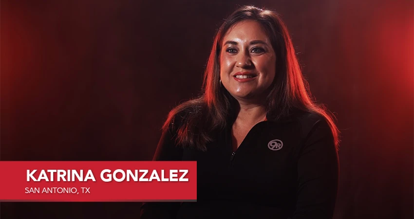 A woman with long brown hair is smiling against a dark, red-lit background. Text on the image reads: Katrina Gonzalez, San Antonio, TX. Her genuine joy reflects her positive franchisee testimonial experience.