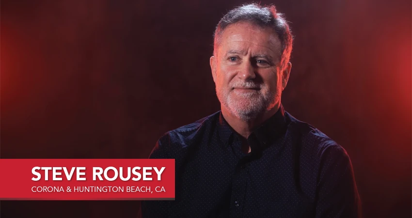 Man with a beard smiling, wearing a dark shirt, stands against a dark reddish background. In a red text box is Steve Rousey, along with Corona & Huntington Beach, CA. This image accompanies his glowing franchisee testimonial.
